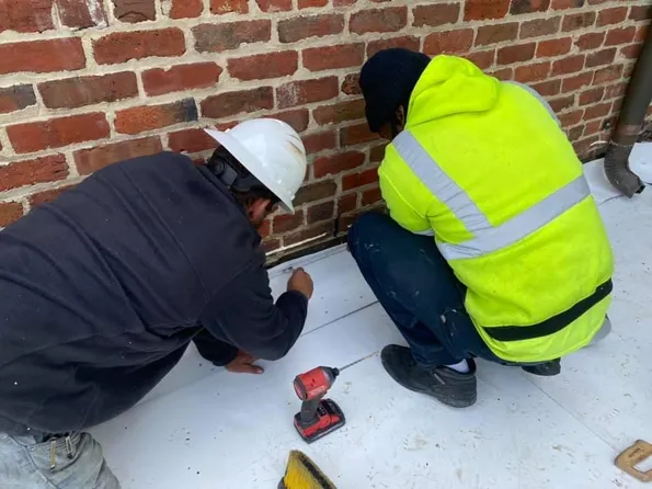two Elevated roofing employees fixing a commercial roof wearing safety gear